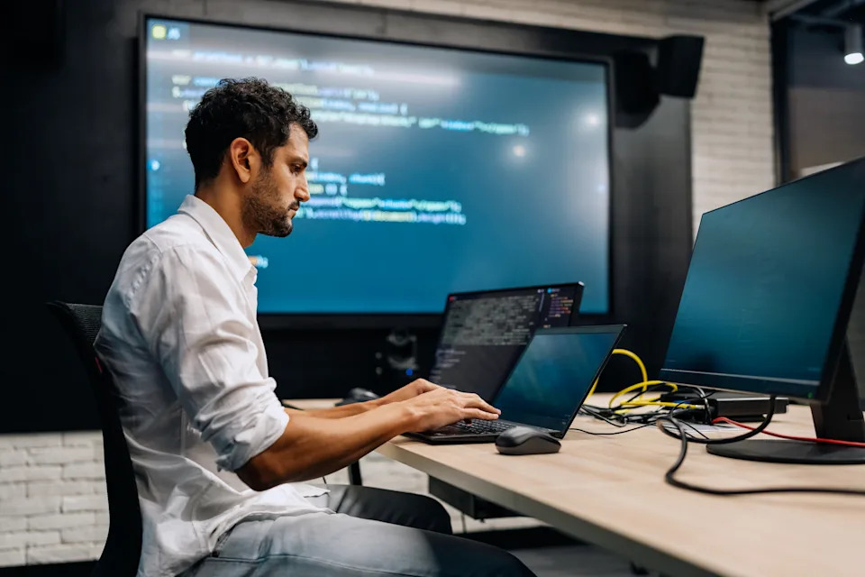 Person in a shirt focuses on programming at a desk with multiple monitors in a modern office setting