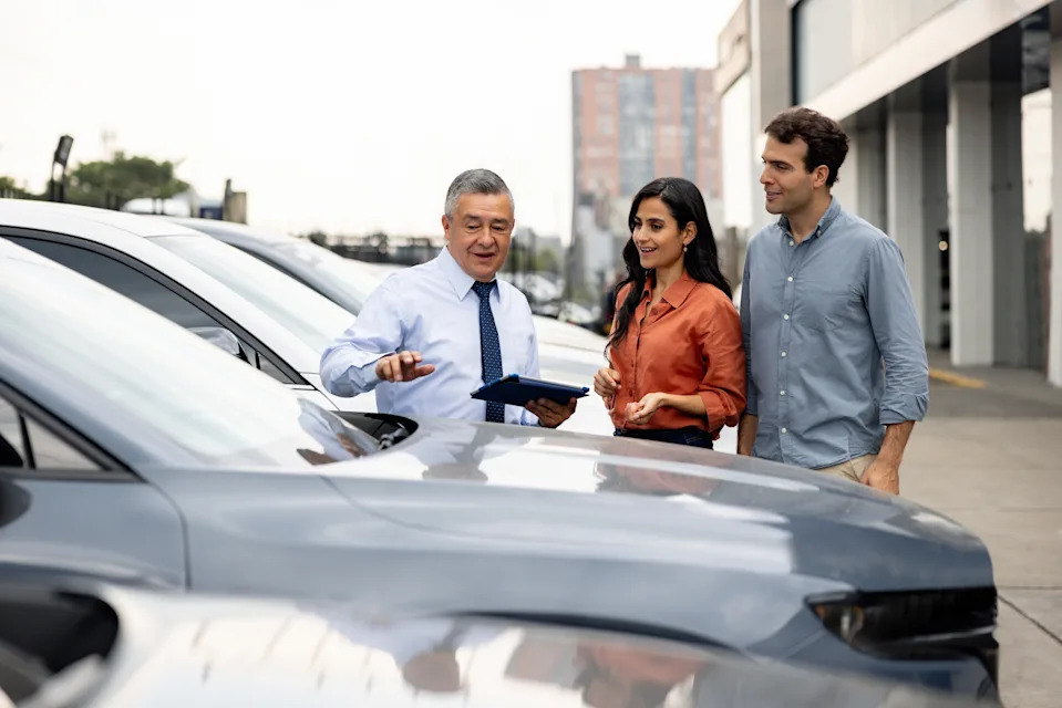 Car sales professional showing a couple a selection of vehicles in a dealership lot, discussing features and options
