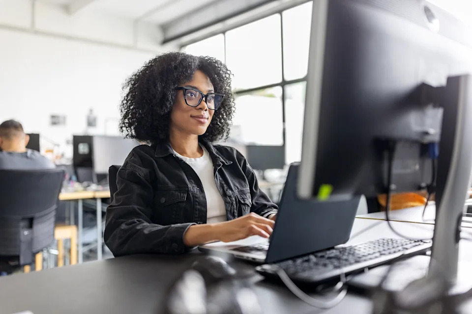 Person wearing glasses and a casual jacket, working at a computer in an office setting