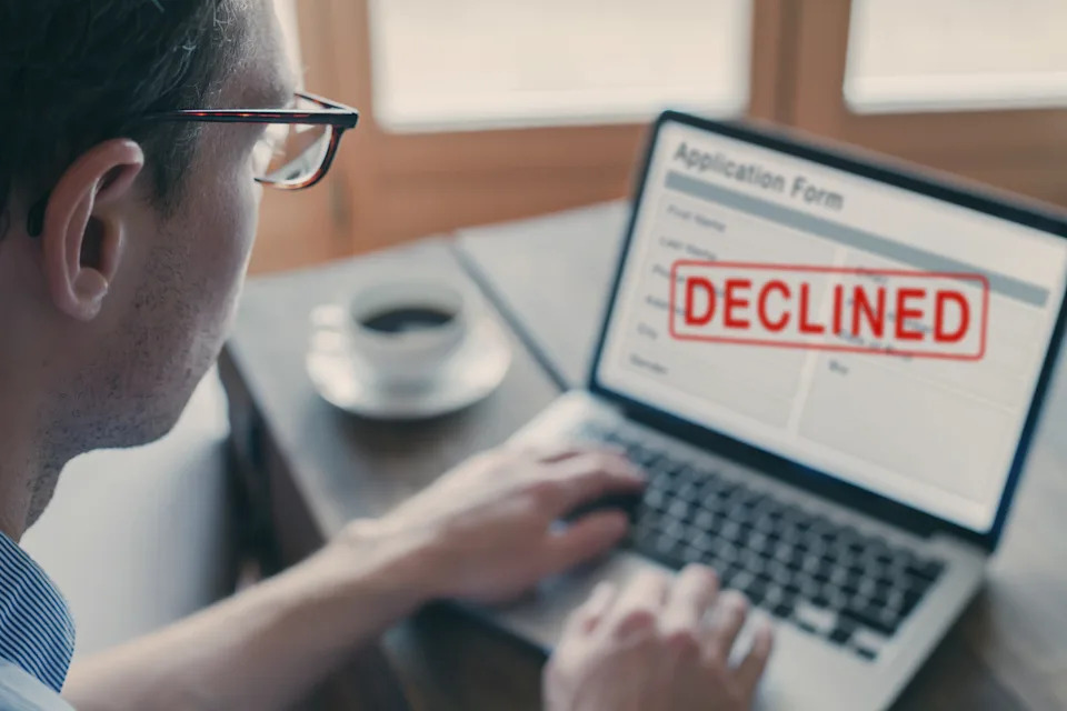 Person viewing a job application form on a laptop with "DECLINED" stamped across the screen