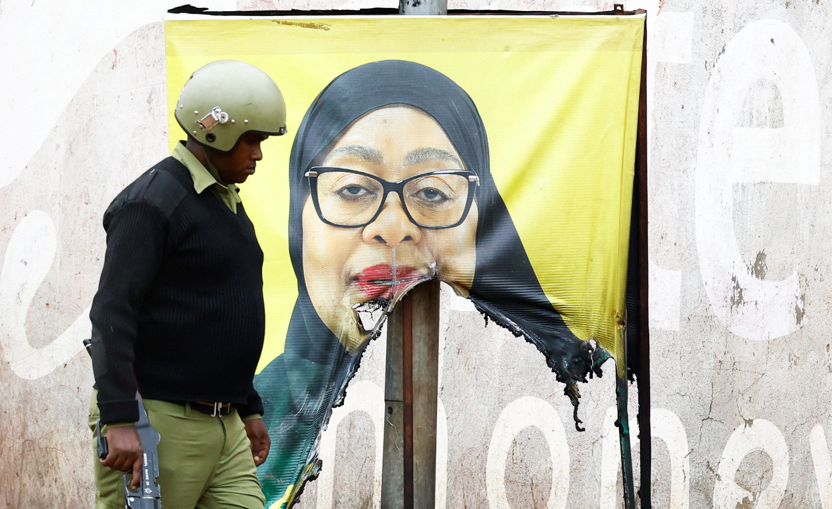 A Tanzanian riot police officer walks past a vandalised campaign poster of President Samia Suluhu Hassan, following a protest on October 30, 2025.(Reuters)