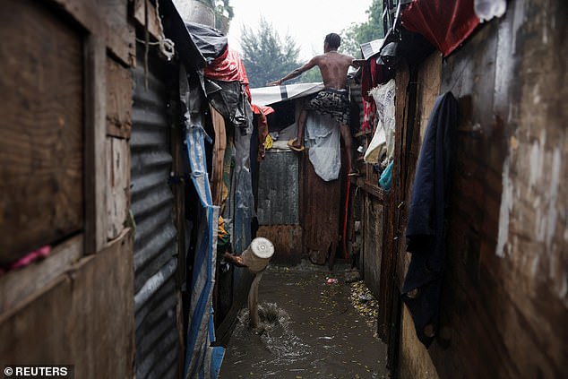 A man climbs onto a shack to inspect a plastic sheet serving as a roof, while another person removes water from their makeshift home during heavy rains brought by the outer bands of Hurricane Melissa, at a Church of Jesus Christ of Latter-day Saints shelter, housing some of the more than 1.3 million Haitians displaced by gang violence, in Port-au-Prince, Haiti October 29, 2025. REUTERS/Claudia Daut