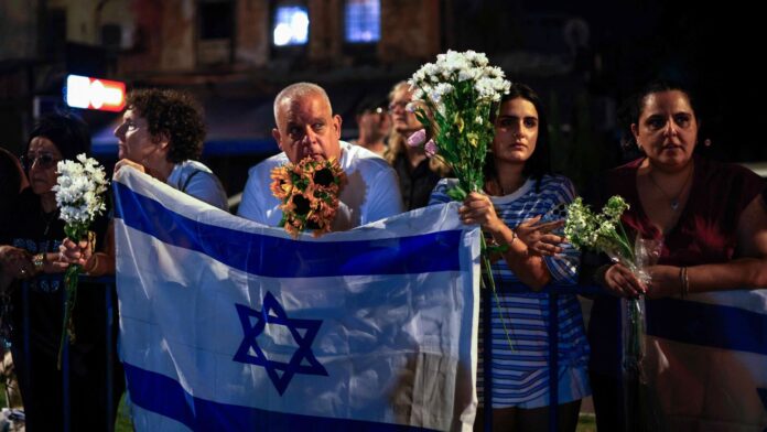 Israel receives four bodies of deceased hostages from Gaza; Hamas People carry flowers and Israeli flags upon the arrival of vehicles transporting the bodies of four hostages handed over following a ceasefire and prisoner exchange deal between Israel and Palestinian factions in Gaza, in front of the National Center for Forensic Medicine in Tel Aviv on October 13, 2025. (Photo by Jalaa MAREY / AFP)