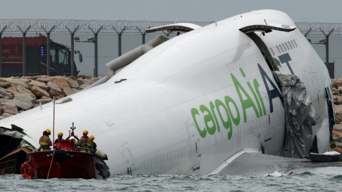 Emergency personnel work near a cargo plane lying partially in the sea after it veered off the runway during landing at Hong Kong International Airport in Hong Kong, China