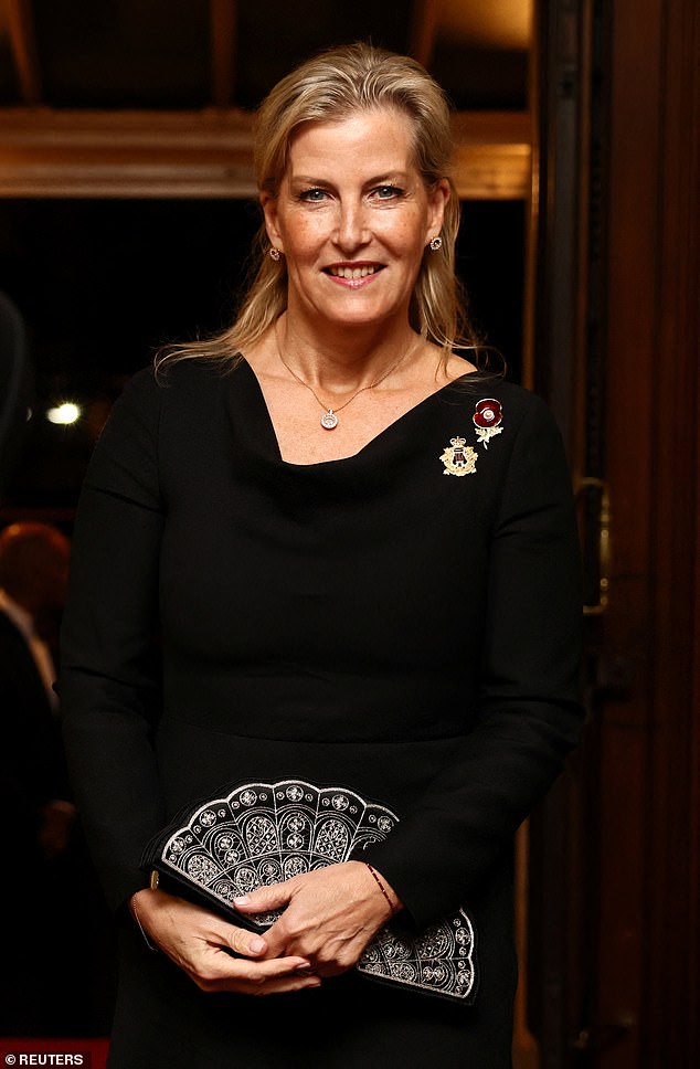 Sophie, the Duchess of Edinburgh, wears a black dress with a statement poppy pin and holds a Lulu Guinness 'Sophie' fan clutch