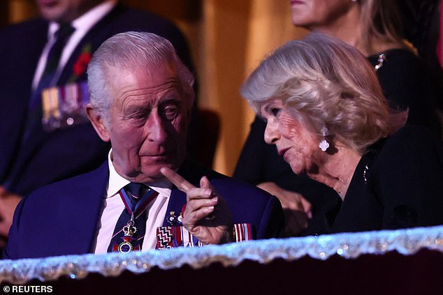 Queen Camilla points something out to her husband King Charles during the performance
