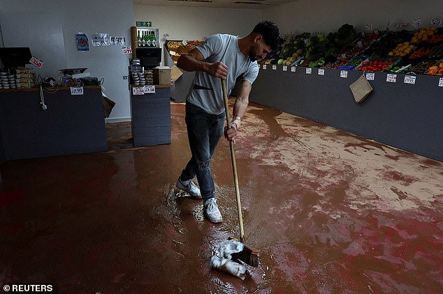 MONMOUTH, NOVEMBER 16: A man sweeps water at a fruit shop after severe flooding caused by Storm Claudia, in Monmouth, Wales